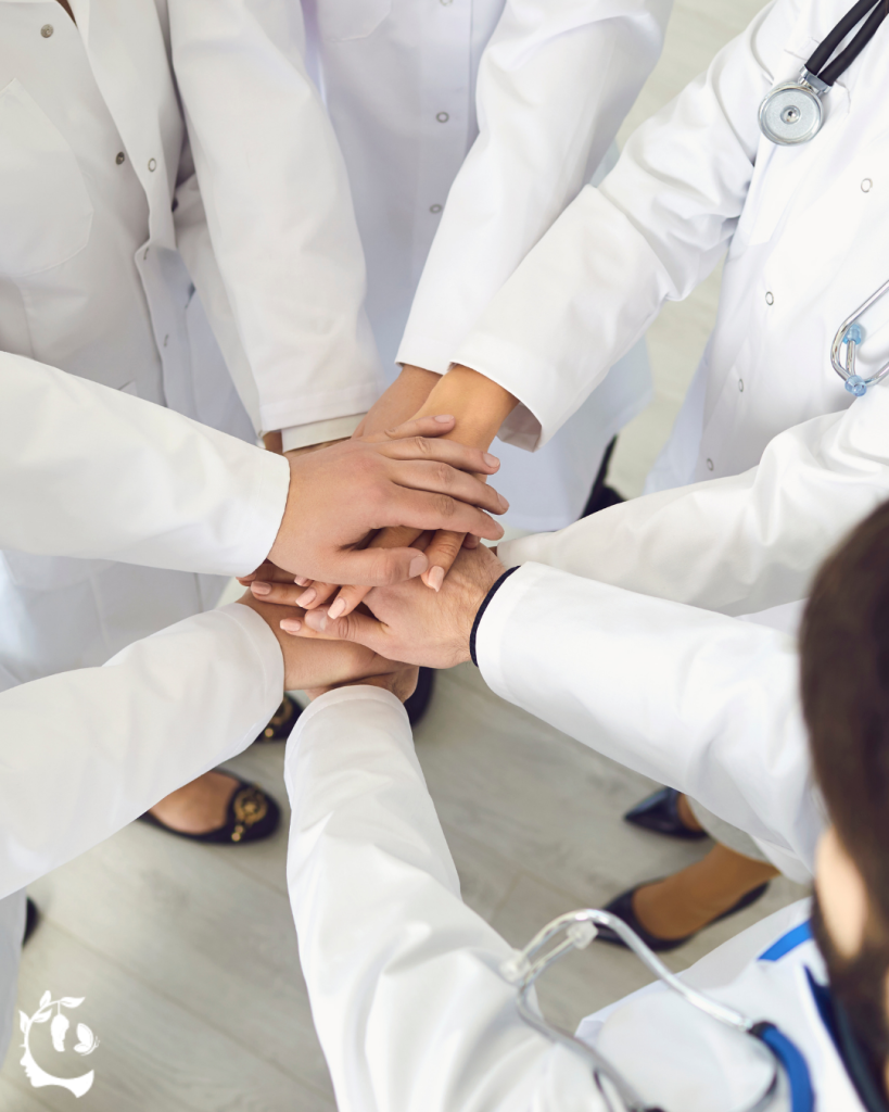 Physicians in white coats stacking their hands together in a circle, viewed from above
