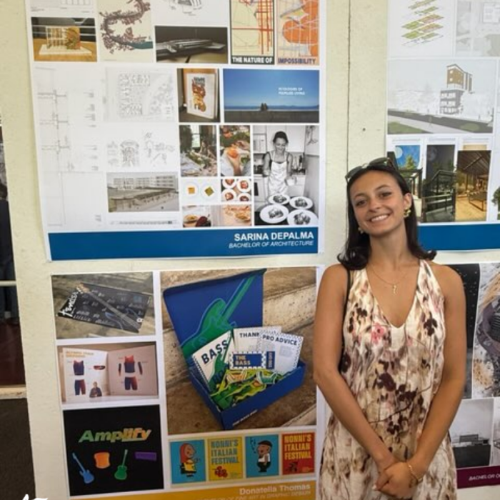 Graduating architecture student standing beside her senior thesis board at a student work exhibition