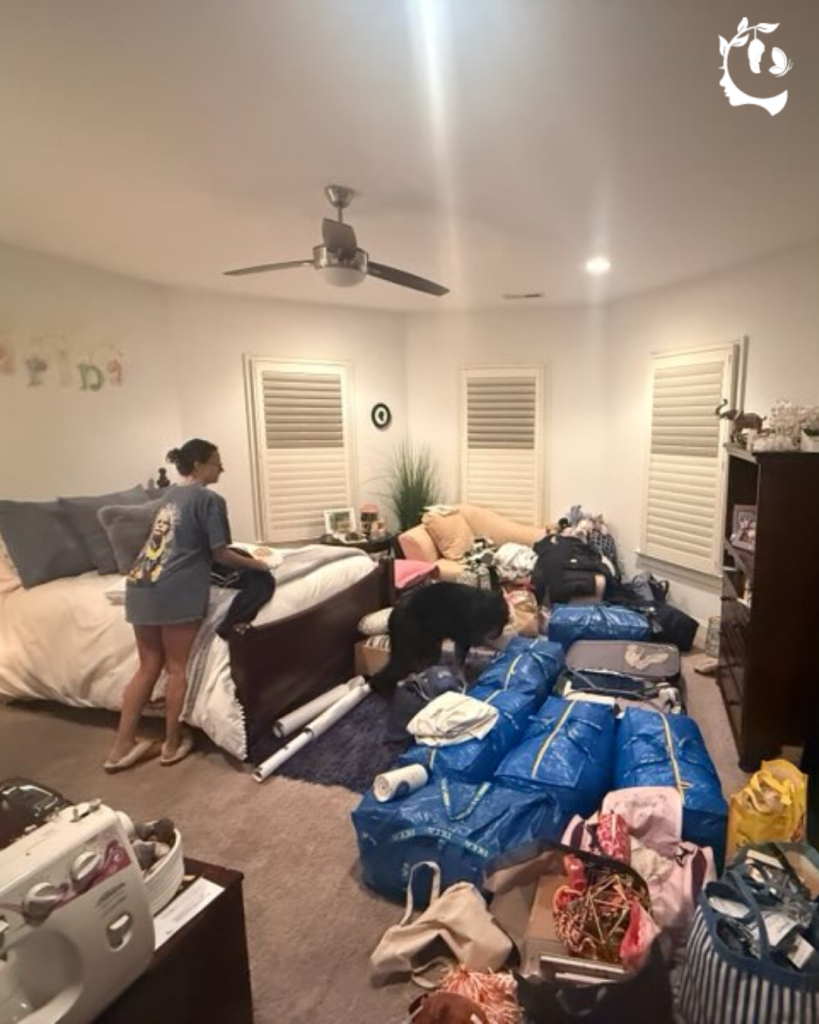 Young woman packing a bedroom filled with blue tote bags and suitcases, with the family dog investigating