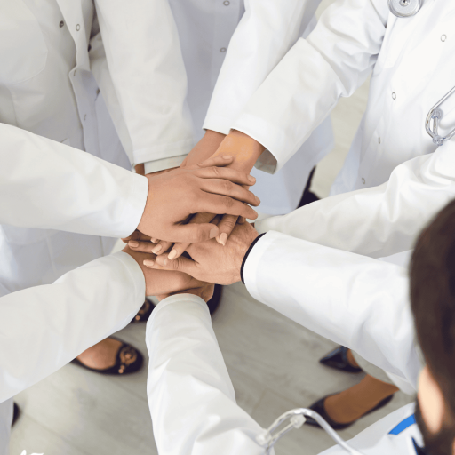 Physicians in white coats stacking their hands together in a circle, viewed from above