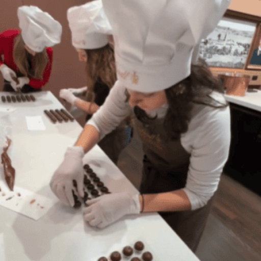 Teen in a chef's hat and apron rolling chocolate truffles at a Lindt chocolate factory workshop