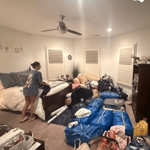 Young woman packing a bedroom filled with blue tote bags and suitcases, with the family dog investigating